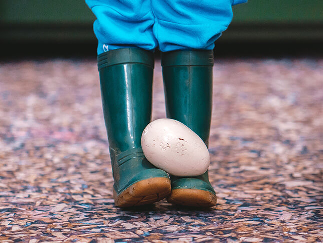 a close up of a child balancing an egg on their feet wearing wellies